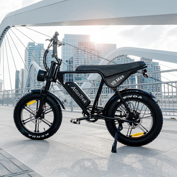 Zwarte AtlasTrek V8 Max elektrische fatbike buiten getoond op een brugpromenade met stadsgebouwen op de achtergrond