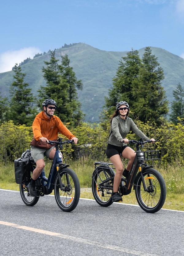 Twee rijders met helm op Engwe E26 3.0 Pro elektrische fietsen die naast een bergvangrail rijden