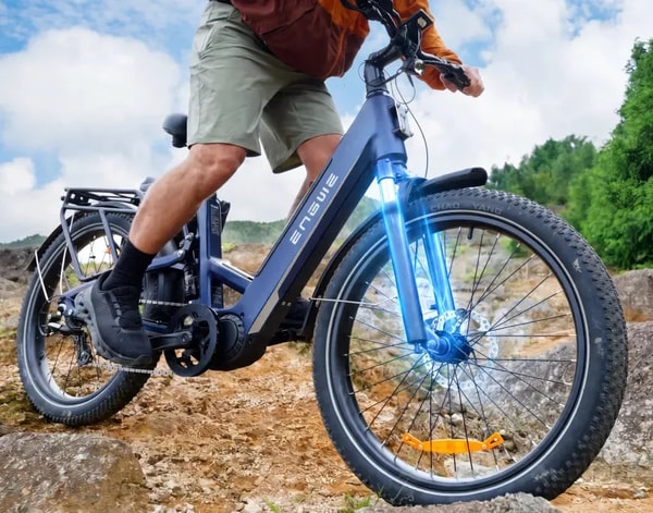 Rijder op een blauwe Engwe E26 3.0 Pro elektrische fiets die rotsachtig off-road terrein doorkruist met de voorvering gemarkeerd