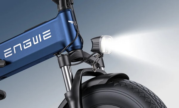 Close-up of the dual-lens LED headlight lit up on the blue Engwe Engine Pro 3.0 Boost, mounted on the front suspension fork above the fat front tire