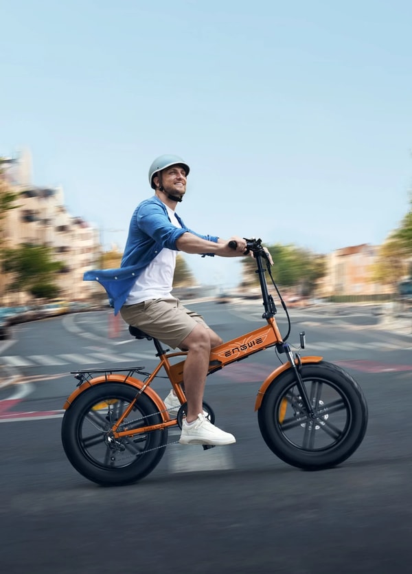 Rijder met helm die een oranje Engwe EP-2 BOOST elektrische fatbike door een stadsstraat rijdt