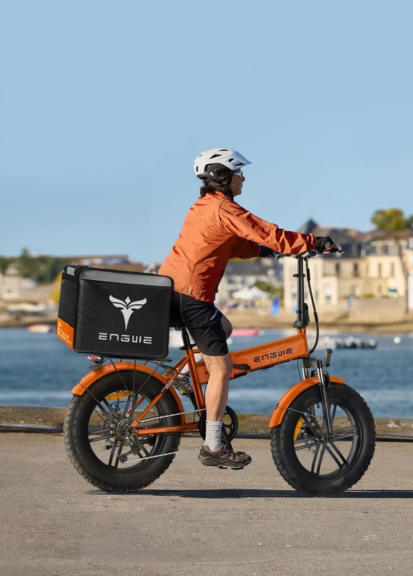 Fietser die een oranje Engwe EP-2 BOOST elektrische fatbike rijdt langs de waterkant met een grote achterste bagagetas