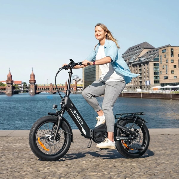 Vrouw die rijdt op een zwarte Engwe L20 3.0 Pro elektrische fiets langs een waterkantpromenade in een stad