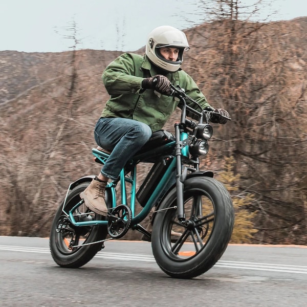 Rijder met helm die op een groene Engwe M20 elektrische fatbike met dubbele accu op een weg rijdt met dubbele koplampen en brede banden